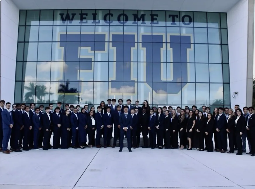 Phoenician Investment Fund members in business attire in front of the Welcome to FIU glass wall
